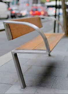 a wooden bench sitting on the side of a street next to a sidewalk with cars in the background