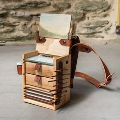 a wooden box with drawers and leather straps on the bottom, sitting on concrete floor