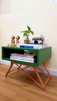 a green table topped with books and a radio next to a plant on top of a hard wood floor