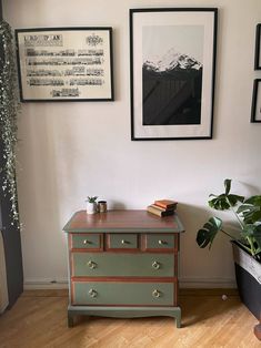 an old dresser is painted green and has pictures on the wall above it, along with a potted plant