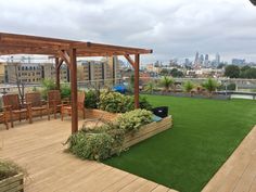 a wooden deck with green grass and plants on the top of it in front of a cityscape