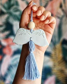 a woman's hand holding a ceramic angel ornament with tassels