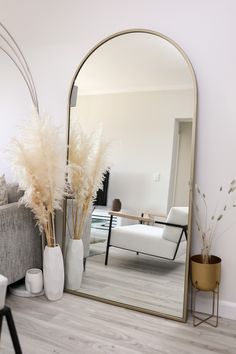 a mirror sitting on top of a wooden floor next to a couch and vases