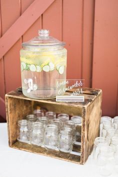 a wooden crate filled with lots of glass jars next to a sign that says lemonade and cucumber water