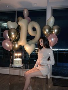 a woman sitting on a chair in front of a cake and balloons that spell the number 19