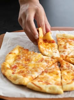 a person taking a slice of cheese pizza from a wooden cutting board on top of a table