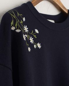 a black sweatshirt with white daisies embroidered on the front and back, hanging from a wooden hanger