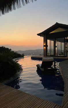 an outdoor swimming pool at dusk with the sun setting in the distance and lights on