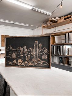 a chalkboard with a cactus drawn on it in front of a bookshelf