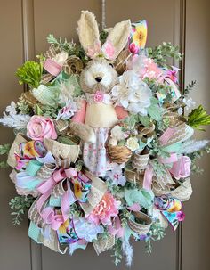 a wreath with a stuffed animal hanging from it's front door decorated with flowers and ribbons