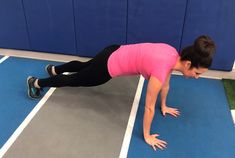 a woman in pink shirt doing push ups on blue and gray floor with wall behind her