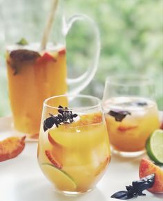 two glasses filled with drinks sitting on top of a white table next to sliced fruit