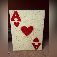 a crocheted card with hearts and two spades on the side, sitting on carpet