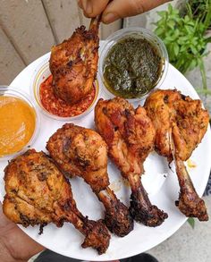 a person holding a plate with chicken wings and sauces on it