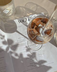 a drink in a glass on top of a table next to a menu and wine glasses