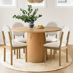 a round wooden table with white chairs around it and a potted plant in the center