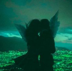 two people standing in front of a city at night with green lights on the ground