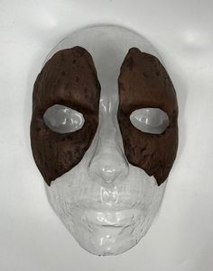 a white and brown mask with holes in it's eyes on a white surface