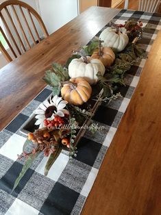 a wooden table topped with lots of pumpkins and flowers on top of a checkered runner