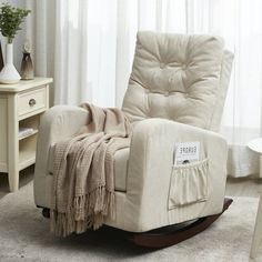 a rocking chair with a blanket on it in front of a white table and window