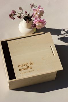 a wooden box with flowers in it next to a white vase on a table top