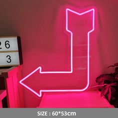 a neon sign with an arrow pointing to the right in front of a pink wall