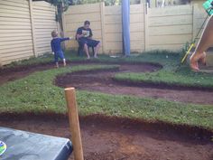 two people sitting on a bench in a backyard with grass and dirt around the yard