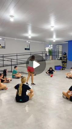 a group of people sitting on the floor in a gym with one person standing up