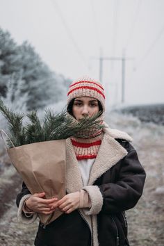 a woman is holding a bouquet and wearing a winter coat while standing in the snow