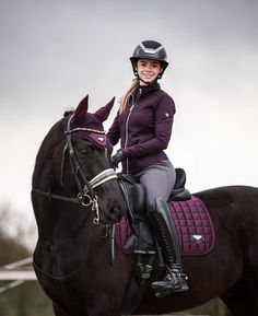 a woman riding on the back of a brown horse wearing a purple jacket and helmet