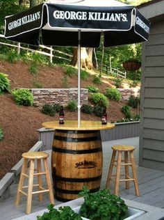 an outdoor bar with two stools under an umbrella on a deck in front of a house