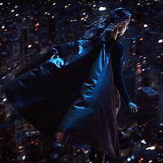 a woman is flying through the air in a dark city at night with lights on