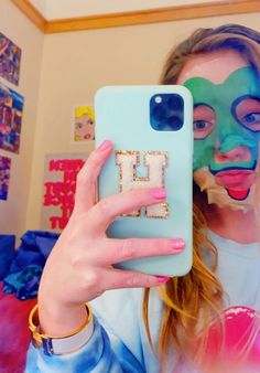 a woman holding up a phone case with the letter l painted on it in front of her face