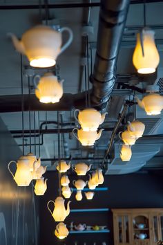 many lights are hanging from the ceiling in a restaurant or bar, which is decorated with teapots and cups