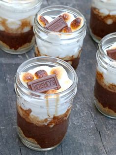 desserts in glass jars with marshmallows and chocolate on top, sitting on a wooden table