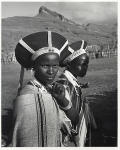 two women wearing hats and scarves on their heads are standing in front of a mountain