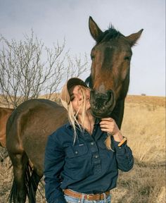 a woman standing next to a brown horse on top of a dry grass covered field