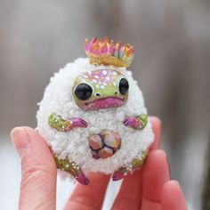 a small toy animal with a crown on it's head sitting in someones hand