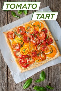 a square pizza topped with tomatoes and basil on top of a piece of parchment paper