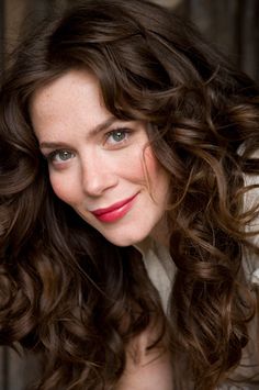 a close up of a woman with curly hair and blue eyes wearing a white shirt