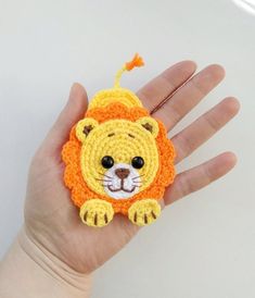 a hand holding a small crocheted lion brooch on it's palm