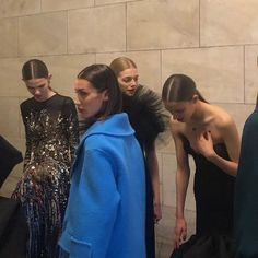 several models stand in front of a wall with their hair pulled back and wearing blue jackets