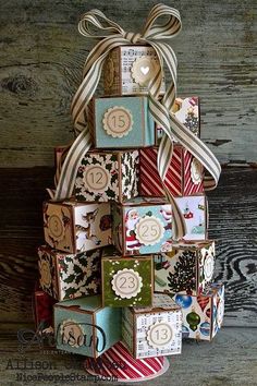 a christmas tree made out of small boxes and ribbon tied around the top, on a wooden surface