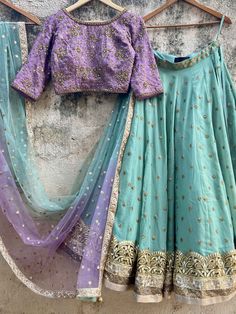 A three-piece sage green and mauve lehenga set from the Priti Sahni collection. This georgette sage green sequin butti lehenga with with a heavy border of sequin, zari work detail is paired with a mauve blouse in sequin, bead and zardozi hand embroidery. The lehenga has side hanging ball tassels to the waistline. And the blouse has a back hook opening. This outfit is completed with a shaded sage green-mauve dupatta in net material with sequin work. Mauve Lehenga, Off Shoulder Lehenga, Royal Blue Lehenga, Mauve Blouse, Ruffle Lehenga, Purple Lehenga, Raw Silk Lehenga, Yellow Lehenga, Wedding Lehenga Designs