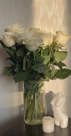 a vase filled with white roses on top of a table next to a candle holder