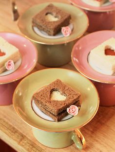 small desserts are arranged in pink and yellow dishes on a wooden table with gold rimmed saucers