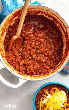 chili and cheese in a pot with a wooden spoon next to it on a table