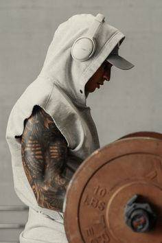 a man in a white hoodie holding a barbell with tattoos on his arm