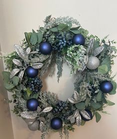 a wreath with blue ornaments and greenery on the front is hung on a wall