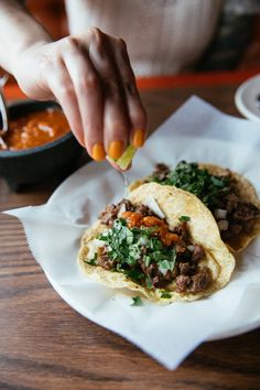 a person is dipping sauce on some tacos